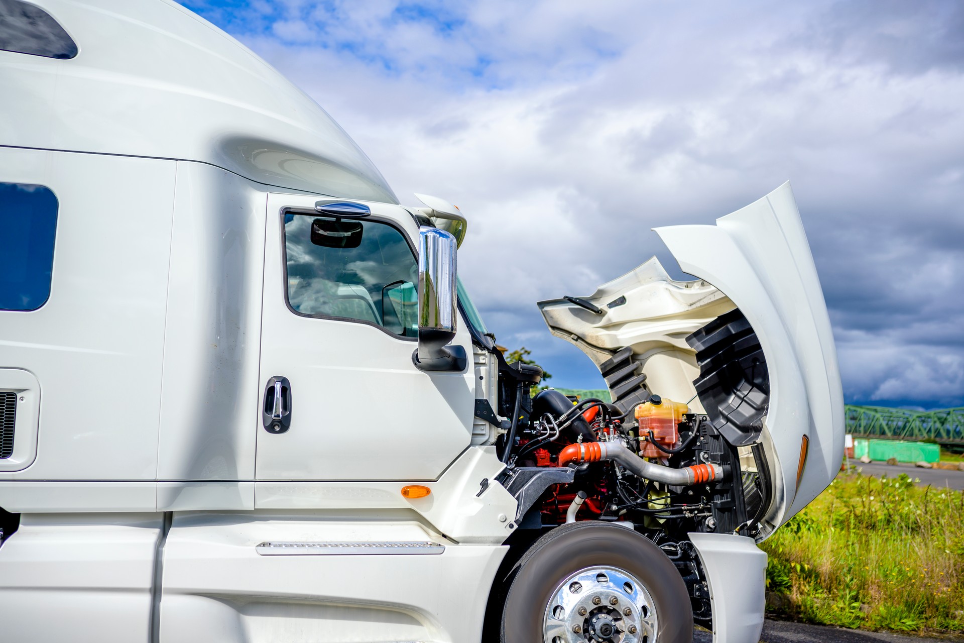 Broken white big rig semi truck tractor stands on the side of the road with an open hood awaiting mobile repair assistance